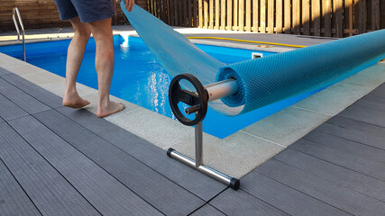 Man covers swimming pool with cover for protection against dirt, leaves, heating and cooling water