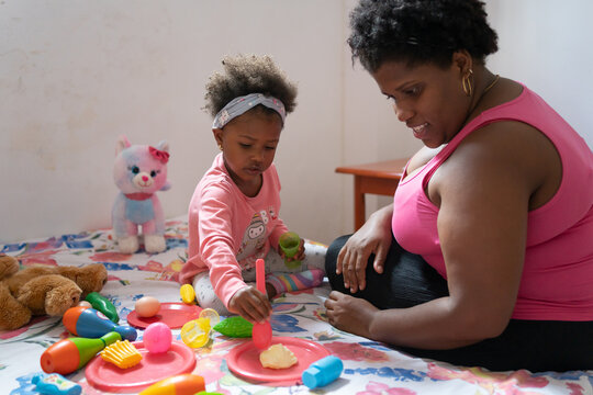 Little Black Girl And Mom Playing With Toys On The Bed.