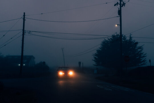 A car driving through a small neighborhood on a foggy evening