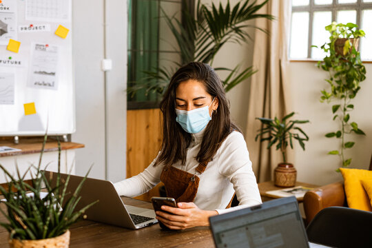 Focused female freelancer working at office wearing protective face mask due to the coronavirus