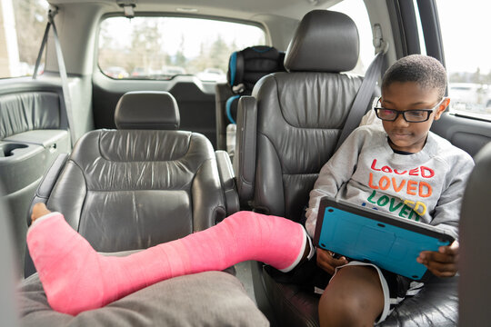 Boy with broken leg sits in van looking at tablet