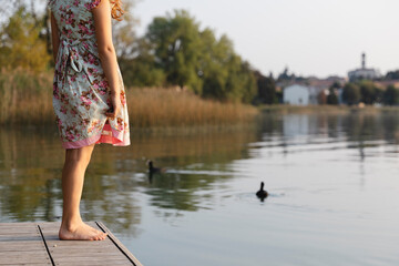 Little girl standing by the lake watching the ducks