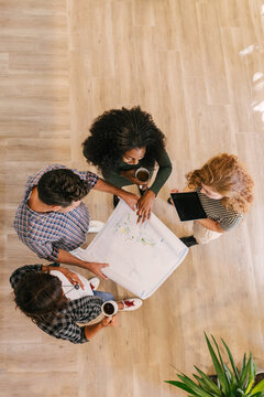 Shot from above of architects reviewing blueprints on a wooden f