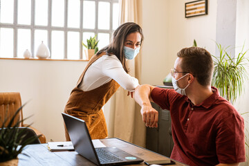 Two coworkers greeting each other in the office protective face mask due to the coronavirus