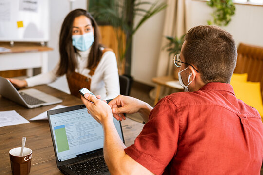Confident female and man freelancer working together at office wearing protective face mask due to the coronavirus