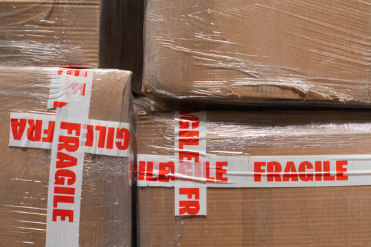 A stock photo close up of cardboard packages wrapped in the protective foil and fragile adhesive warning tape