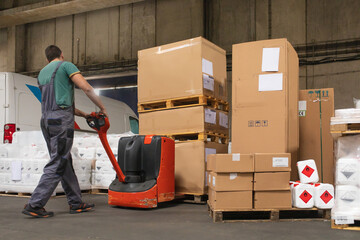 One man operates the pallet jack in a warehouse full of shipping goods