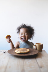 smiling baby girl eating pancakes at breakfast table
