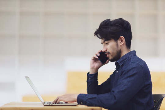 Asia man holding using mobile phone and working on laptop.