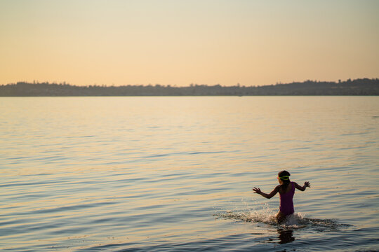 Silhouette of girl wading into bay at sunset