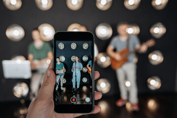 Crop person recording video of musicians on smartphone