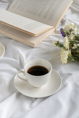 Cup of coffee and book on the white bed. Morning 
