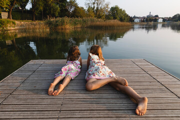 Little sisters lying together look at the lake