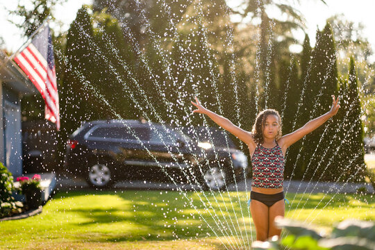 Curly haired girl stands in sprinkler with arms raised