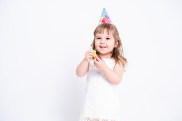 Fototapeta na wymiar Funny child girl in white dress and birthday hat blowing in whistle on white background