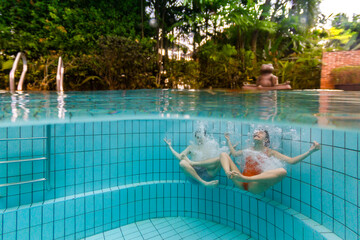 Two friends playing around in a residential pool. They are having fun under water emulating a lotus position.