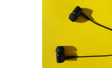 Black headphones on a yellow background, bright light and hard shadow, the concept of using the modern social app Clubhouse on a smartphone, white negative space on the left