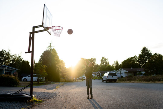 Mixed race boy shooting hoops at sunset in cul du sac