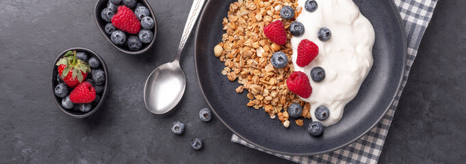 Horizontal banner with homemade granola, yogurt and fresh berries in black ceramic plate on dark stone background. Healthy vegan breakfast - Image
