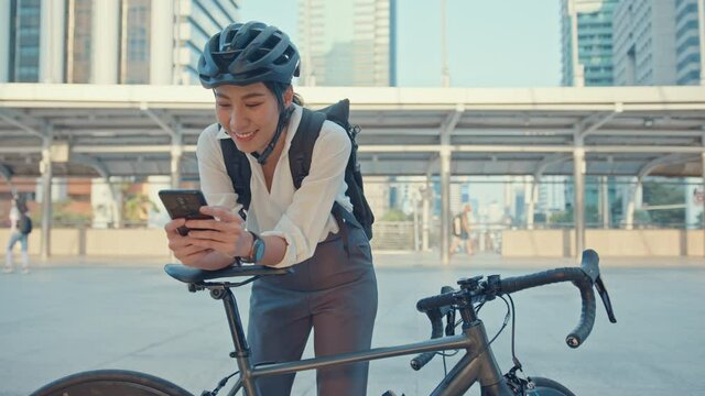 Smile  asian businesswoman with backpack use smart phone look camera in city stand at street with bike go to work at office. Sport girl use phone for work. Commute to work, Business commuter in city.