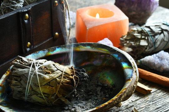 A close up image of a burning white sage smudge stick and healing crystals. 