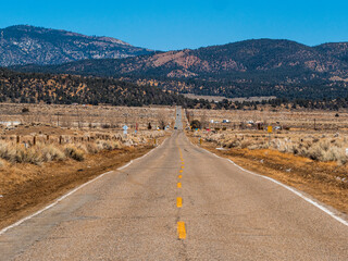 Looking Down The Middle Of A Long Asphalt Country Road Towards Mountains