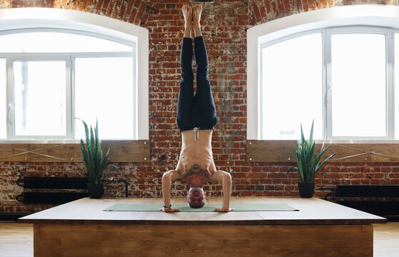 Shirtless man doing Tripod Headstand on platform