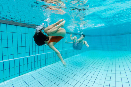 Two friends playing around in a residential pool. They are underwater doing flips.