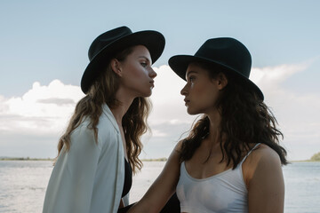 Two girls in hat near the river bank look at each other