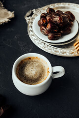 freshly brewed coffee with foam, dried dates on vintage dishes oriental in dark atmosphere. oriental sweets, honey honey stick, grain burlap cloth. oriental holiday layout, vertical, selective focus
