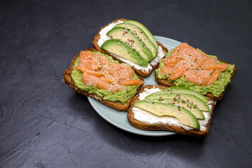 Homemade sandwich with trout, guacamole. Four delicious toast with rye bread, avocado, smoked salmon on dark concrete background. Set of various danish open sandwiches. Healthy food, breakfast concept