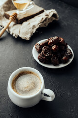 oriental style coffee: freshly brewed drink with foam, dried dates in a vintage plate, honey. dark mood image. food content. vertical, selective focus