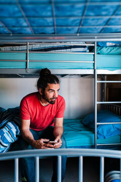 Traveler using smartphone on bunk bed in hostel