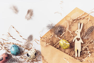 Easter eggs, hare, feathers, hay in a craft envelope on a white background. Holiday message happy Easter, correspondence concept. Flat lay, top view. Easter card