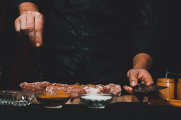 Marinating pork neck skewers, adding salt, curry and basil to the meat, pieces of meat on a wooden board.