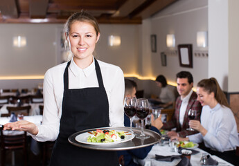 Attractive waitress with serving tray welcoming to cozy restaurant