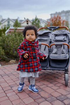 a little girl is standing next to a large double stroller
