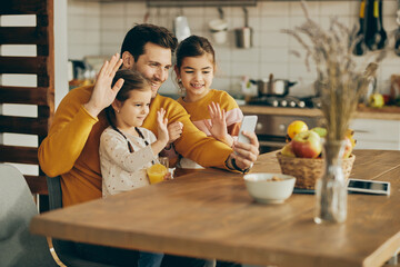 Happy family waving during video call over smart phone at home.