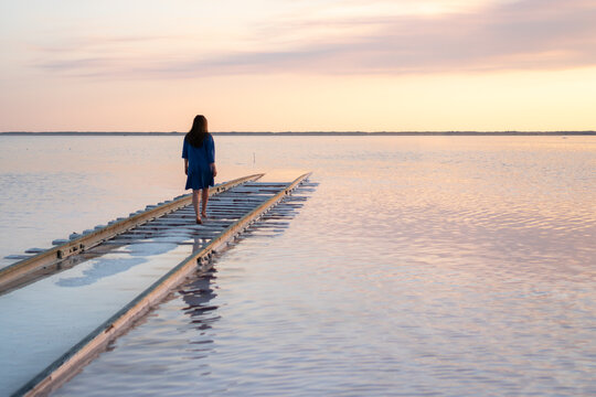 Girl standing on railway going into a Pink lake at sunset