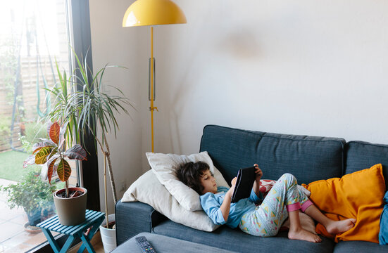 Kid laying on the couch playing with an electronic device at home