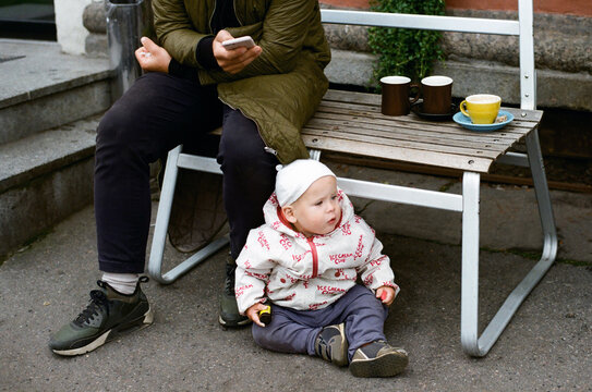 Toddler sitting on the pavement next to father&rsquo;s legs