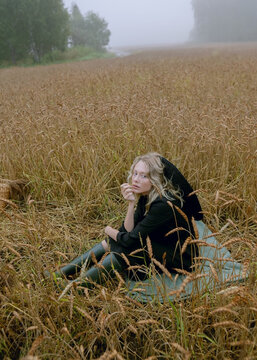 girl in black clothes and hat sitting in a wheat field and posing