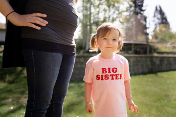 Cut toddler in big sister smiles at camera next to pregnant mom