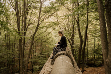 Young woman sitting in old pipeline drawing in notebook in forest during autumn
