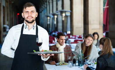 Portrait of glad cheerful positive smiling waiter with serving tray meeting restaurant guests