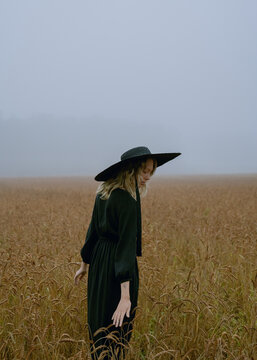 girl in a hat and black dress posing in a wheat field, foggy and mystical atmosphere