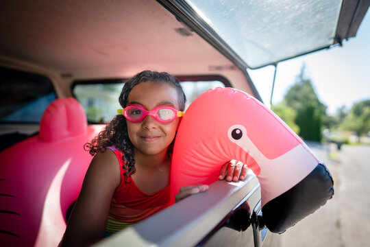 Girl in goggles and swimsuit poses with flamingo floatie in back of truck