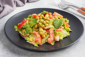 Salad of green tomato leaves and canned peas seasoned with sauce on a black plate. Spring fresh diet salad.