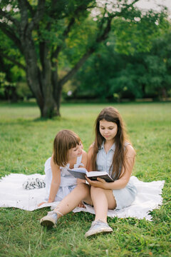 Happy sisters reading book in park