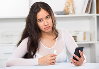 Upset young female sad with mobile phone on sofa indoors